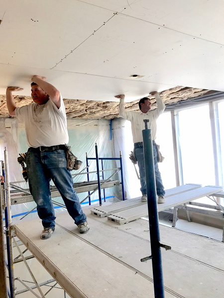 Installing drywall in the storefront. Two workers on a tall scaffold drywall the ceiling