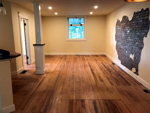 Living are of the manager's suite, showing the beautiful refinished floor, nice lighting, window overlooking the storefront, and the irregular bare patch on the wall showing the original brickwork underneath