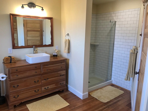 Manager suite bathroom has white subway tile shower with glass door, six-drawer vanity hickory vanity, big white sink, modern comforts that retain the old flavor.
