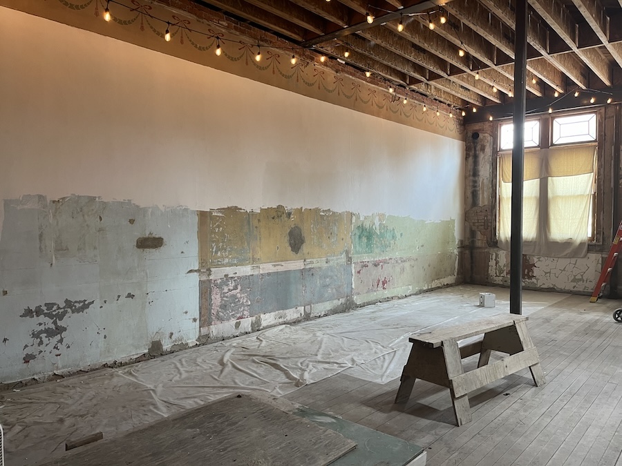 The dining room walls half-plastered. The top half is a nice creamy white. The bottom half is a patchwork of colors and repairs.